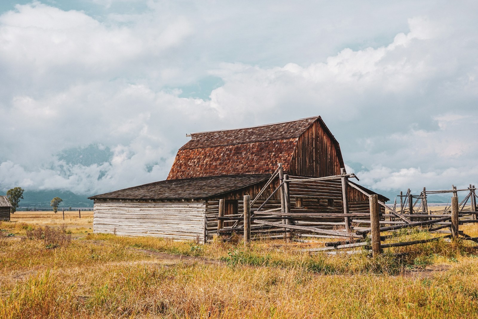 Weathered wooden barn and corral fence in golden grass under a cloudy sky