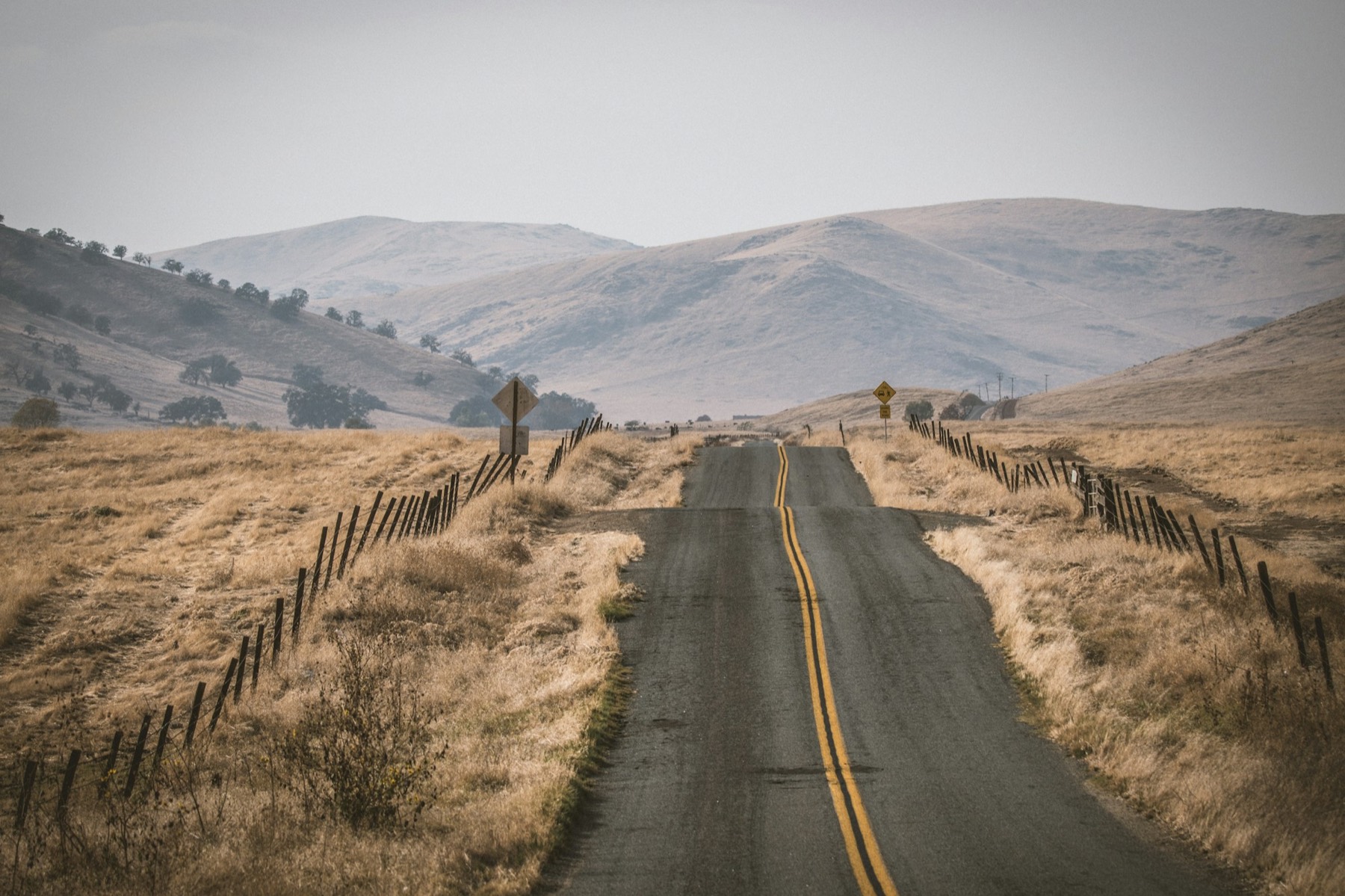 A two-lane rural road through golden rangeland and rolling hills